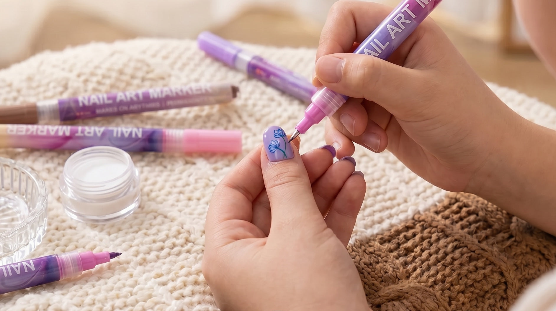 Örgü battaniye üzerinde nail art kalemleri ve çiçek deseni çizilen tırnak